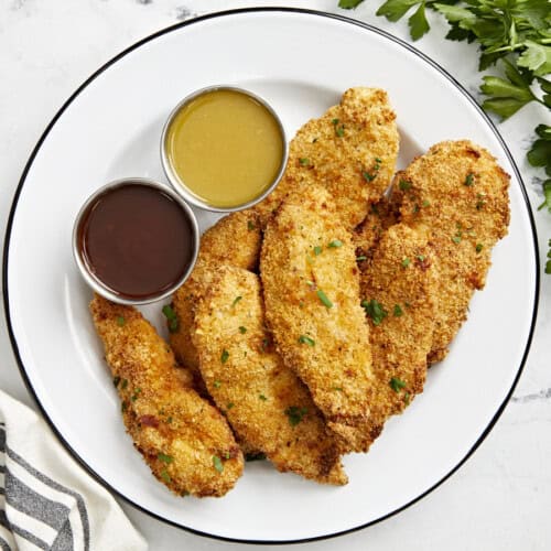 Overhead view of Air Fryer Chicken Tenders on a white serving plate with two dipping sauces on the side.