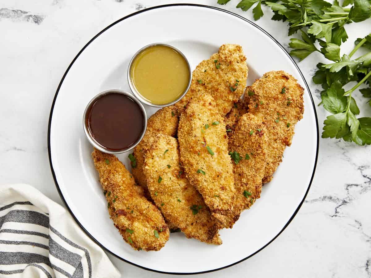 Overhead view of Air Fryer Chicken Tenders on a white serving plate with two dipping sauces on the side.