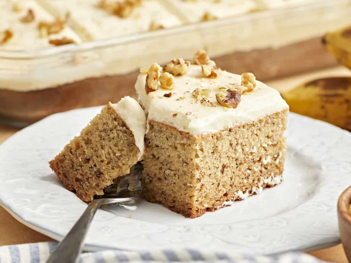 side view of a slice of banana cake on a white plate with a fork.