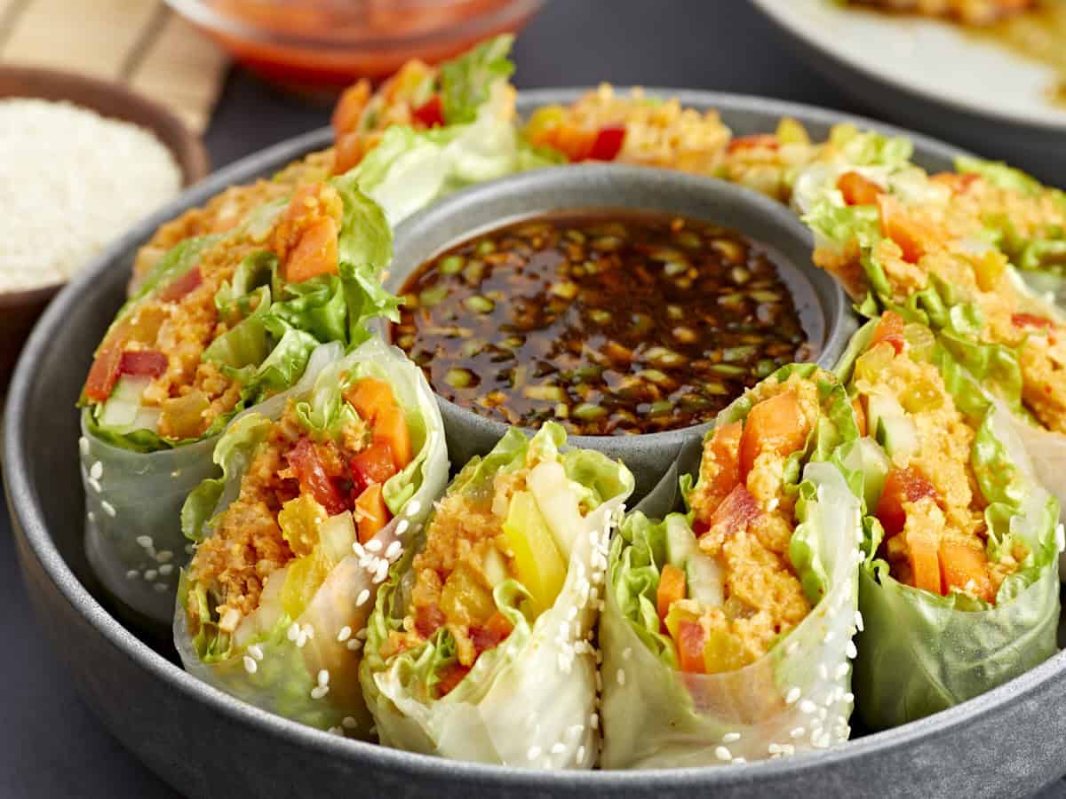 side view of kimchi spring rolls on a platter with a bowl of sauce in the middle.