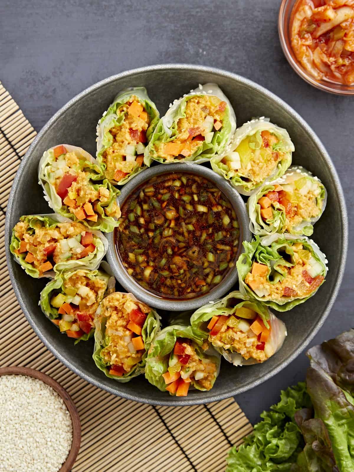overhead view of kimchi spring rolls on a platter with a bowl of sauce in the middle.