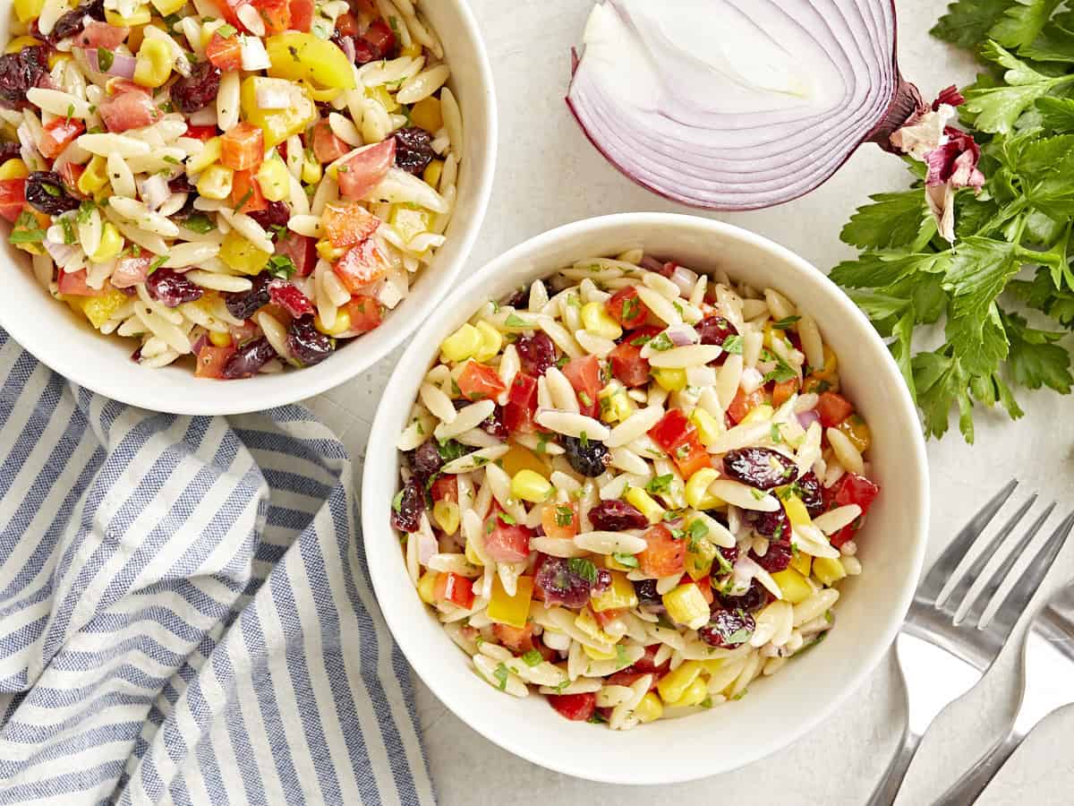 Overhead view of two white bowls of orzo pasta salad.