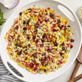 Overhead view of Orzo Pasta Salad in a white serving bowl with wood serving spoons on the side.