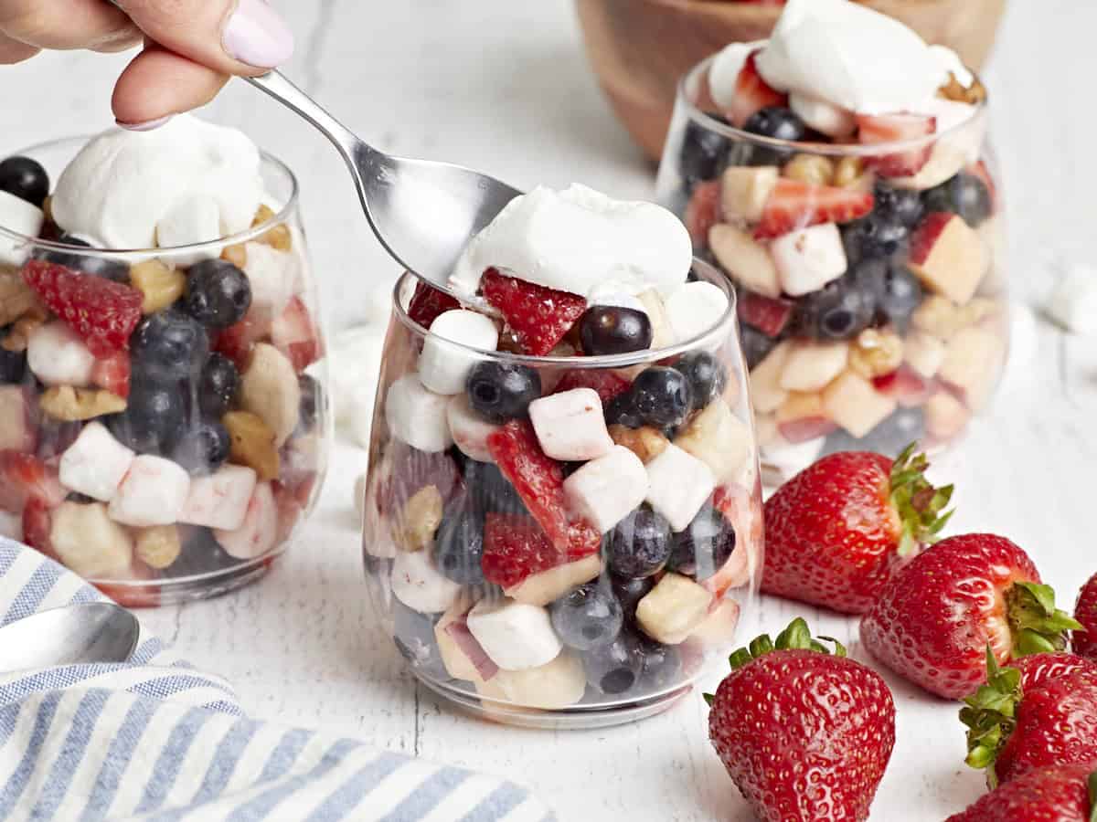 scooping a bite from a serving of red white and blue fruit salad in a stemless wine glass.