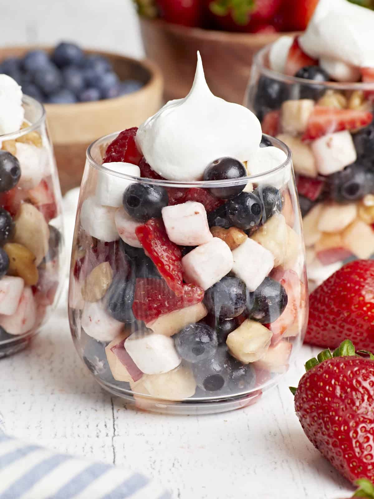 close-up side view of a serving of red white and blue fruit salad in a stemless wine glass with cool whip.