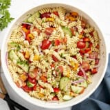 Overhead view of pasta salad in a large white serving bowl with wood serving utensils on the side.