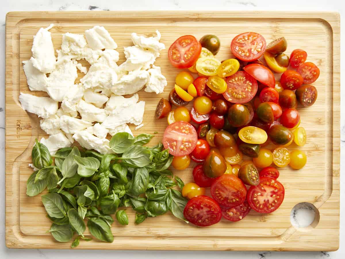 torn mozzarella, basil leaves, and halved tomatoes on a cutting board.