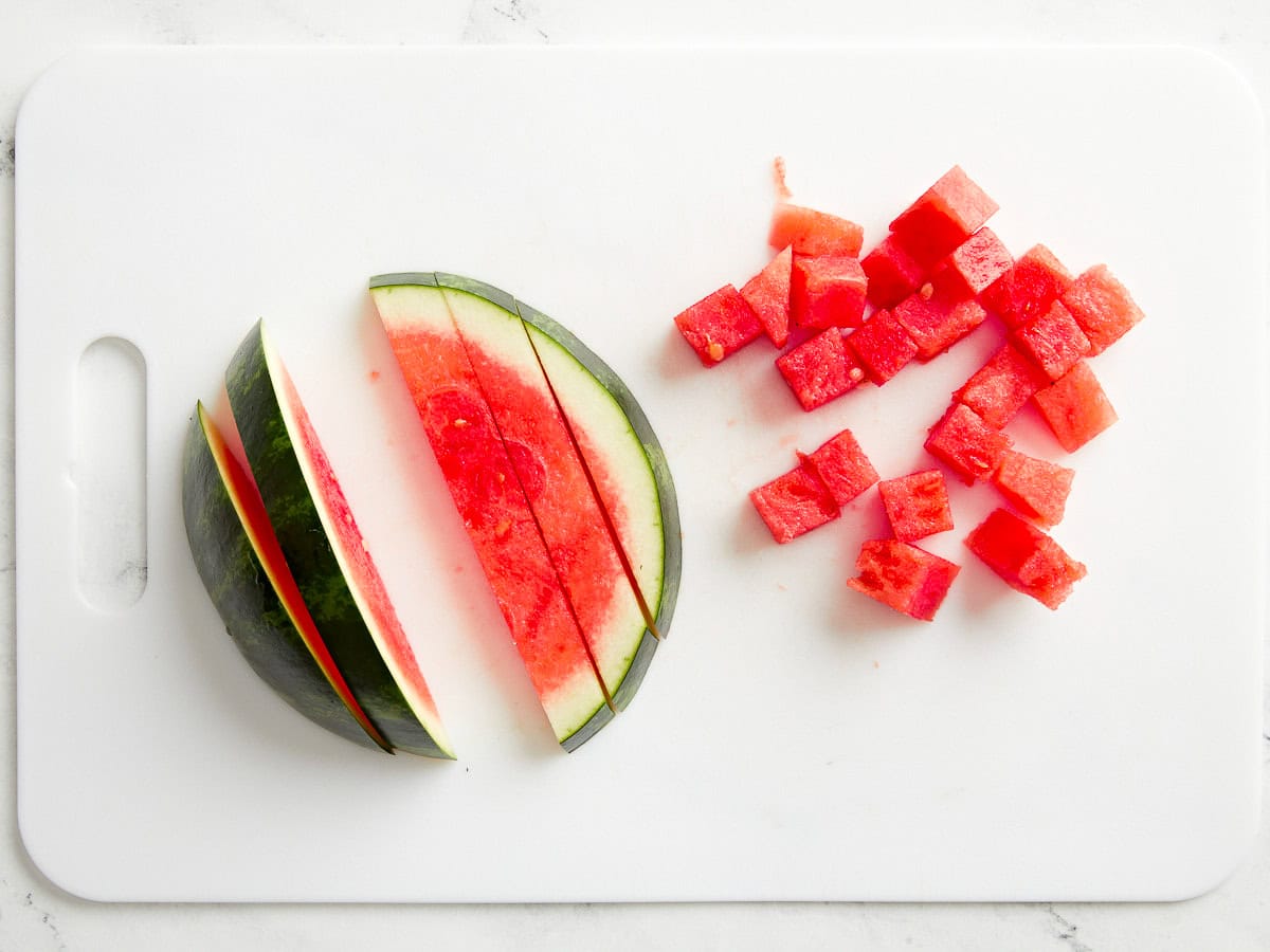 partially diced watermelon on a white cutting board.