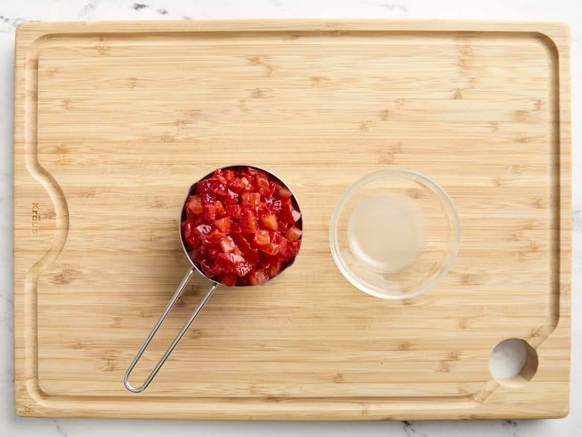 diced strawberries in a measuring cup next to a small bowl of lemon juice on a cutting board.
