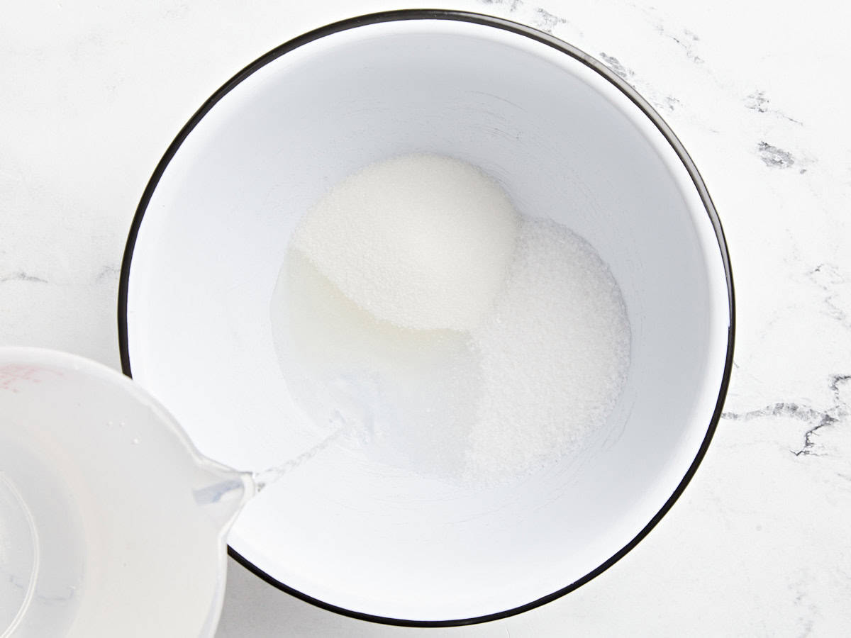 pouring water over sugar and salt in a large white bowl.