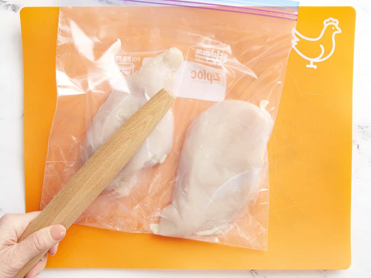 pounding chicken breasts in a ziplock bag with a rolling pin.