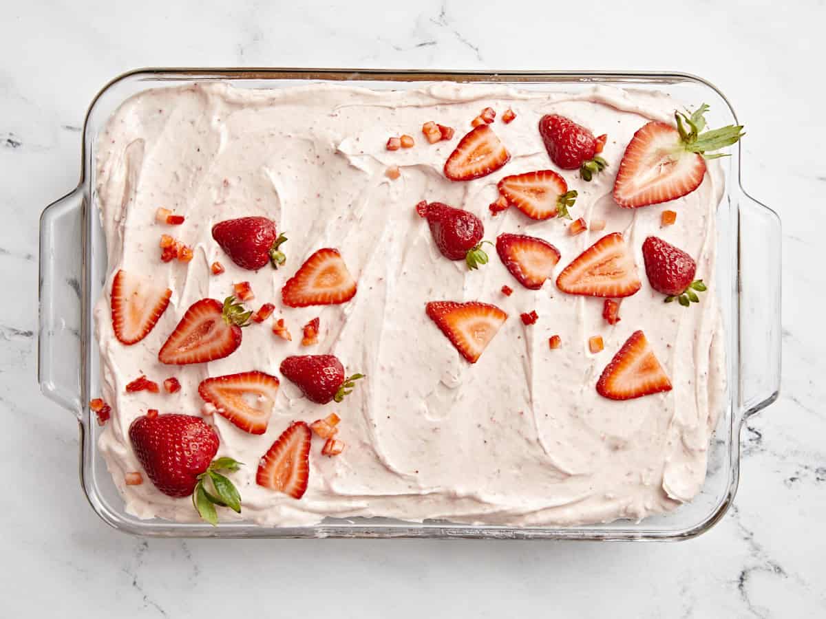 Overhead view of strawberry sheet cake with strawberry icing and fresh strawberries on top.
