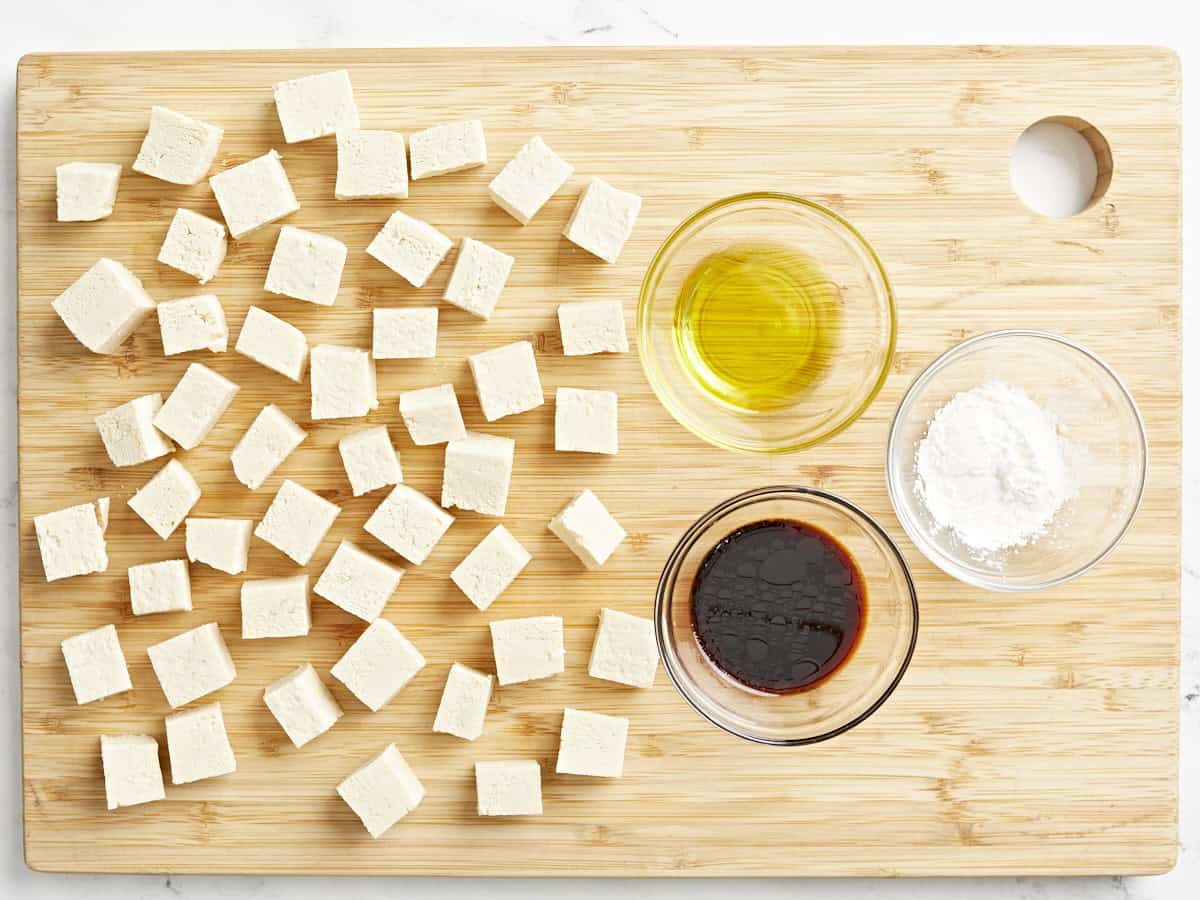 diced tofu next to bowls of sesame oil, soy sauce, and cornstarch on a cutting board.