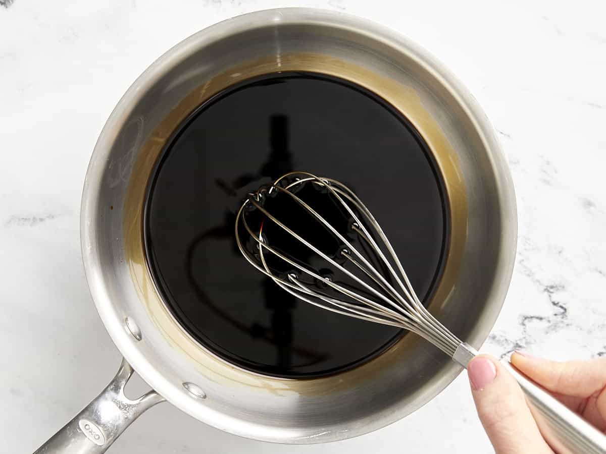 whisking balsamic glaze in a saucepan with a whisk.