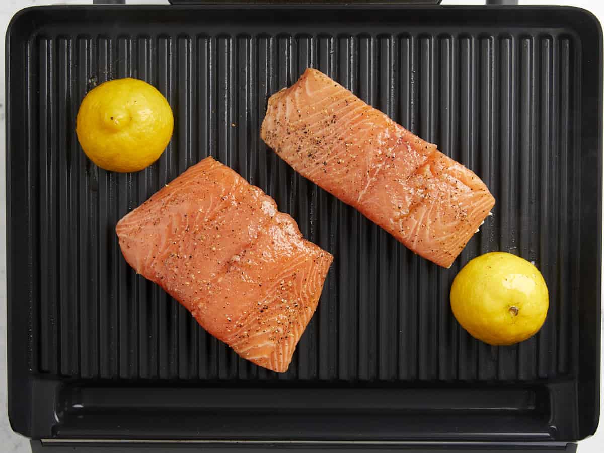 2 salmon fillets and lemon halves on a grill pan.