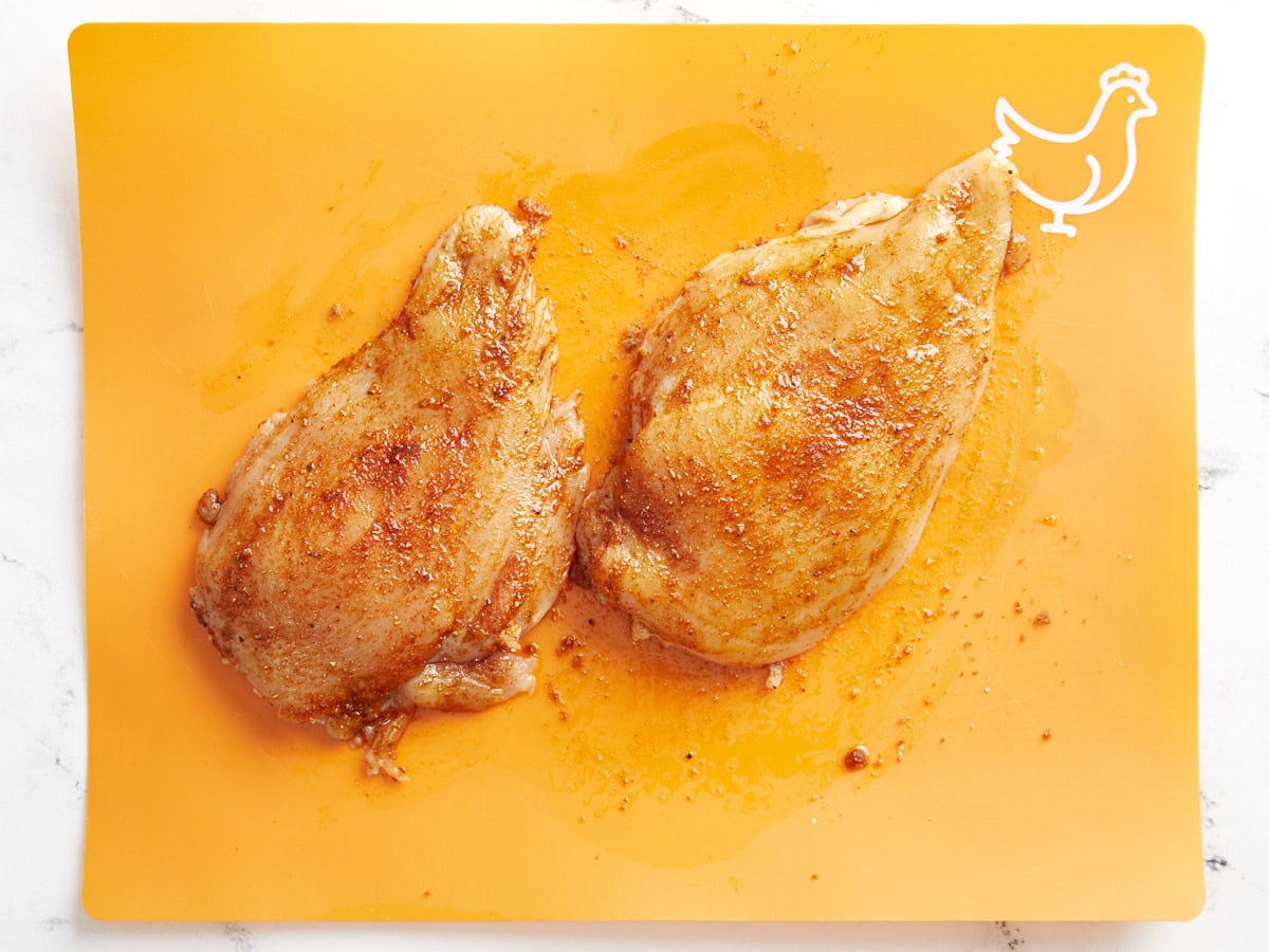 seasoned raw chicken breasts on an orange cutting board.