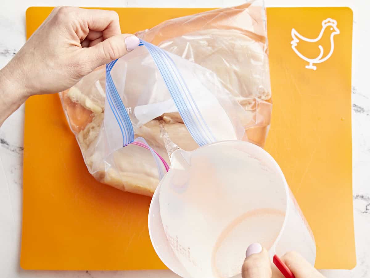 pouring brine into a ziplock bag with chicken breasts.