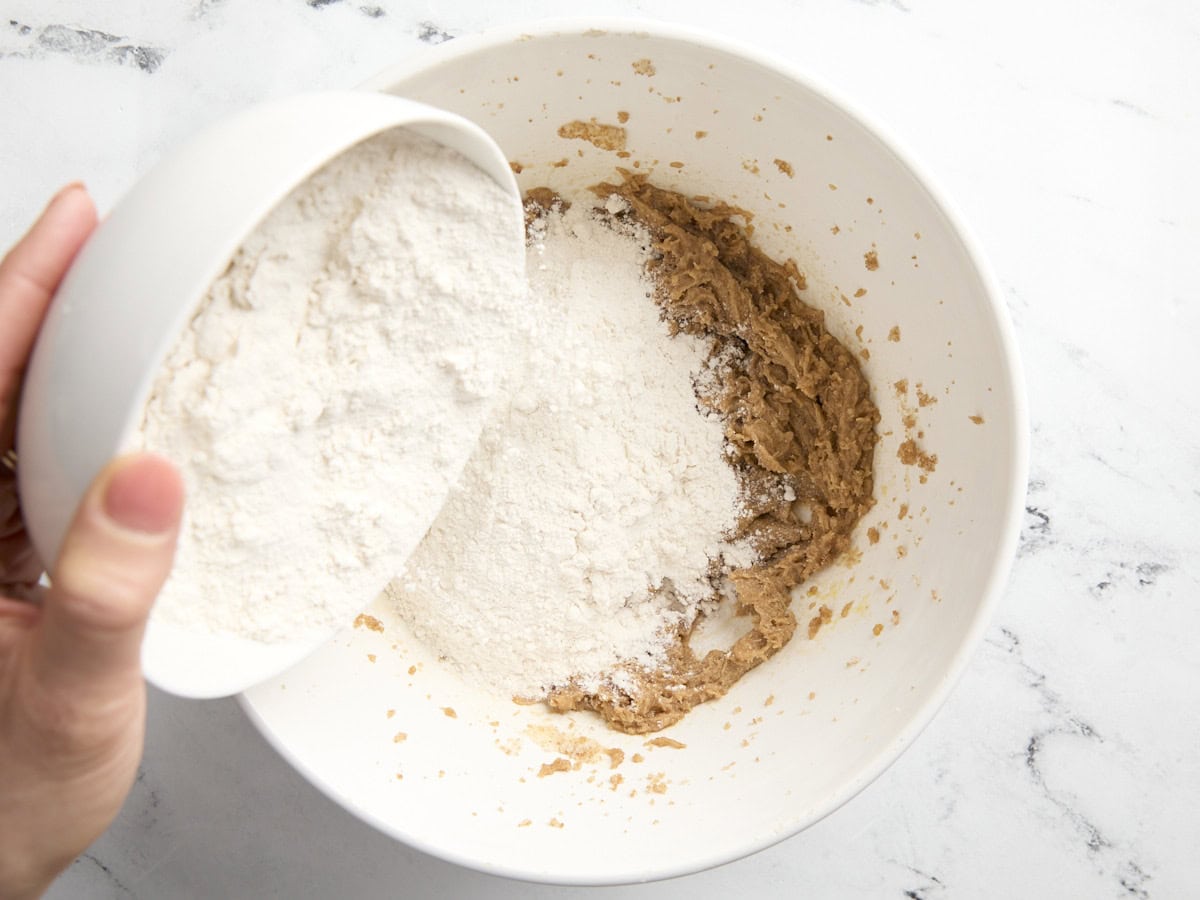 adding dry ingredients to wet in a white bowl.