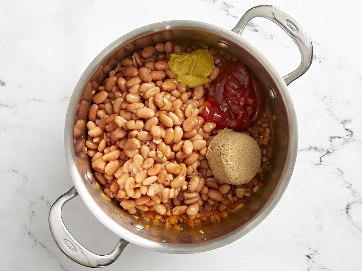 beans, brown sugar, ketchup, and mustard added to a pot with sautéed onions.