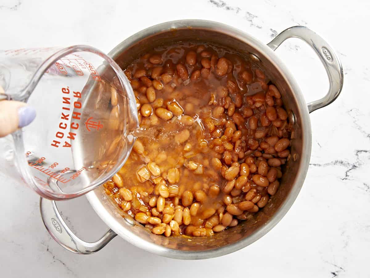 pouring water over stovetop baked beans in a pot.