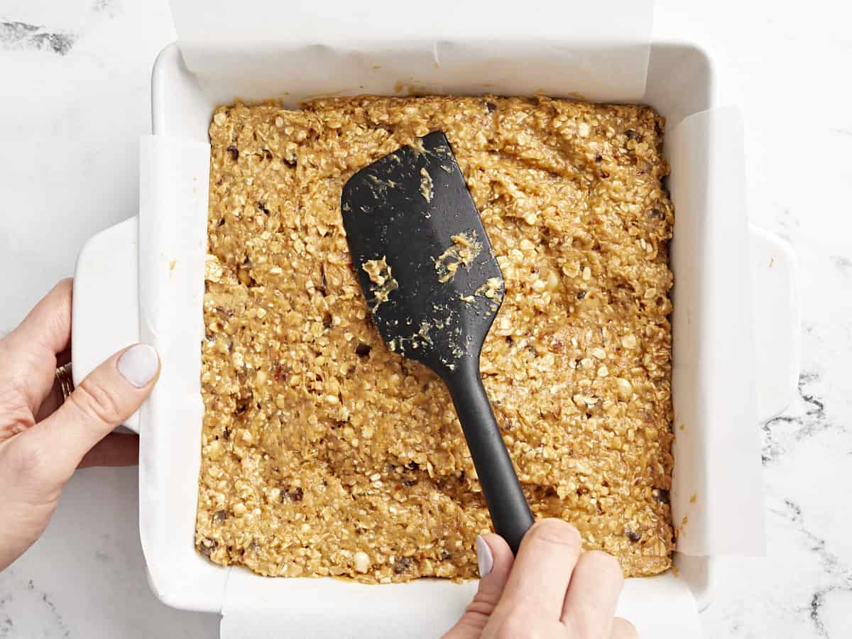 spreading granola bar mix into a baking pan with a rubber spatula.