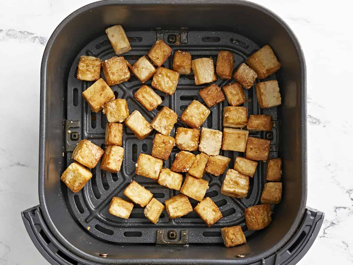cooked crispy tofu cubes in an air fryer basket.