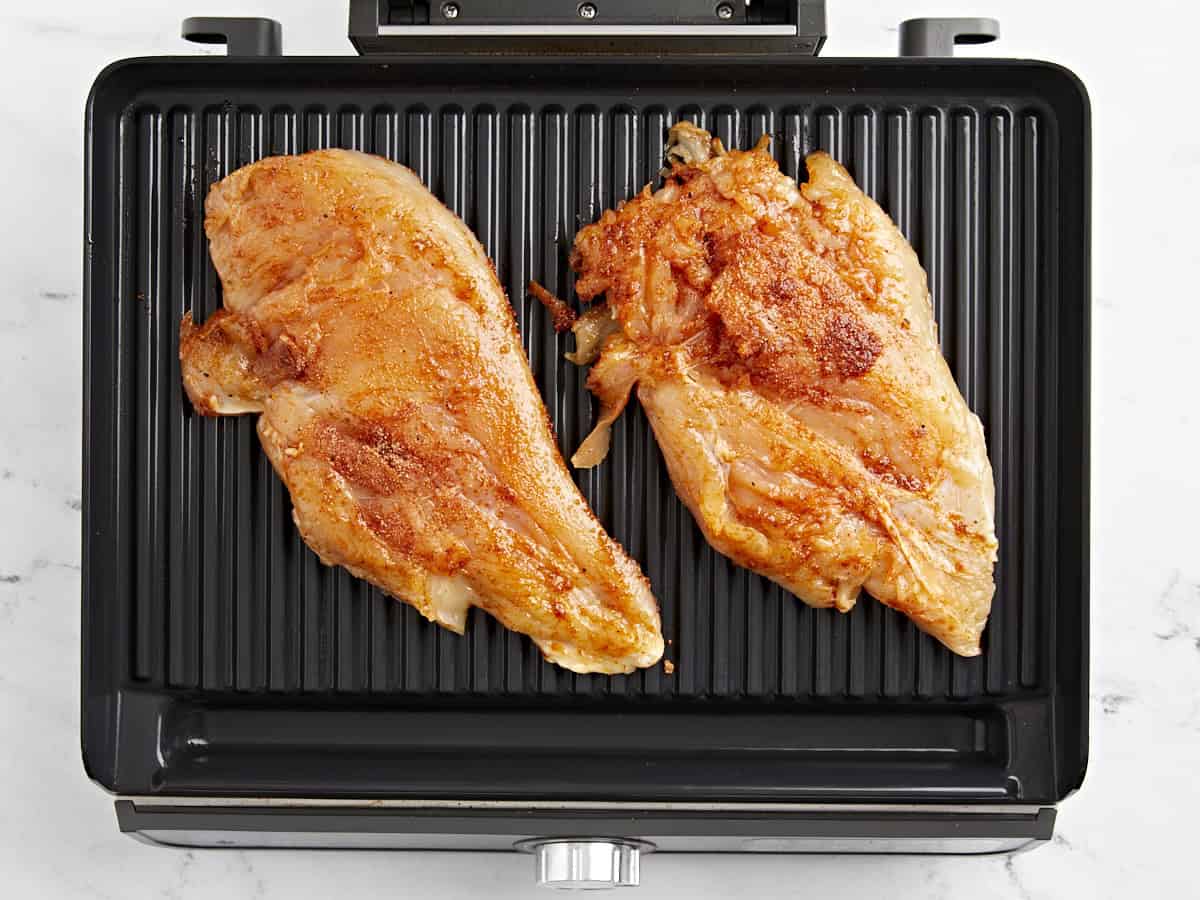 2 raw chicken breasts on a grill.