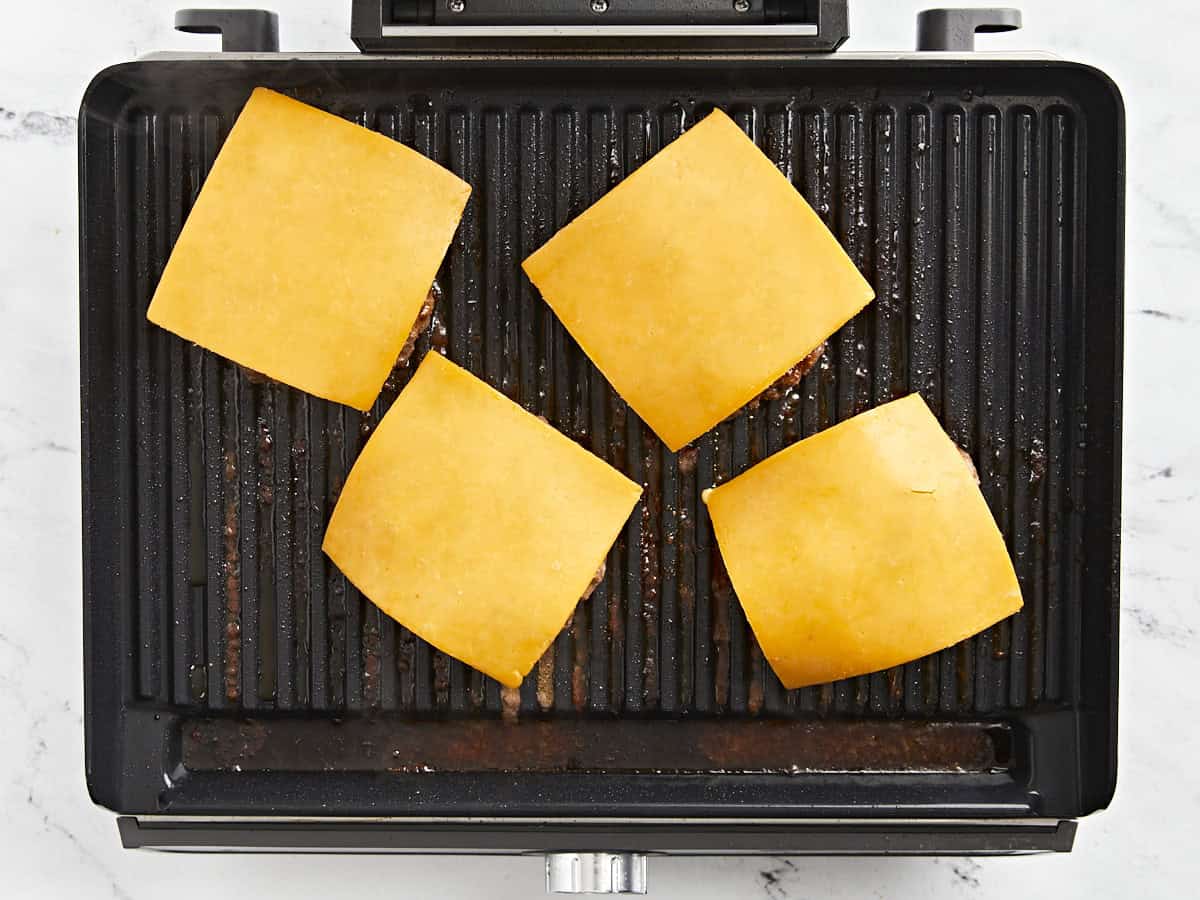 Hamburger patties with cheese on top on the grill.