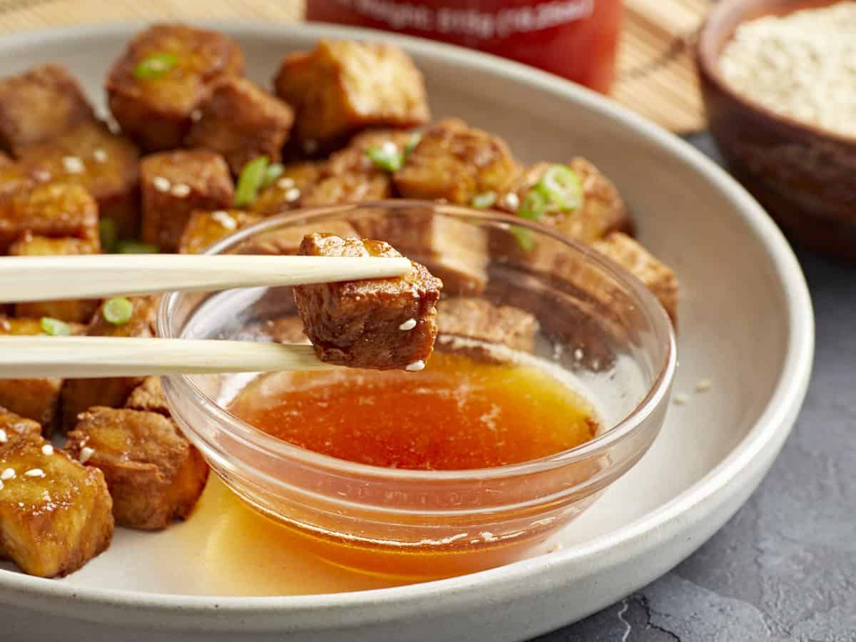 dipping a cube of air fryer tofu in sweet chili dipping sauce with chopsticks.