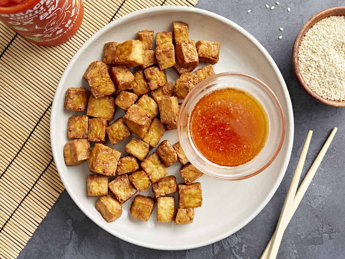 overhead view of air fryer tofu with sweet chili dipping sauce on a white plate.