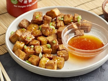 air fryer tofu on a white plate with a bowl of sweet chili dipping sauce.