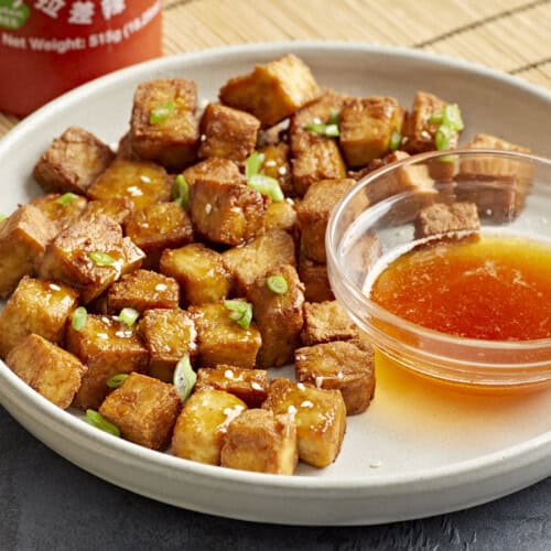 air fryer tofu on a white plate with a bowl of sweet chili dipping sauce.