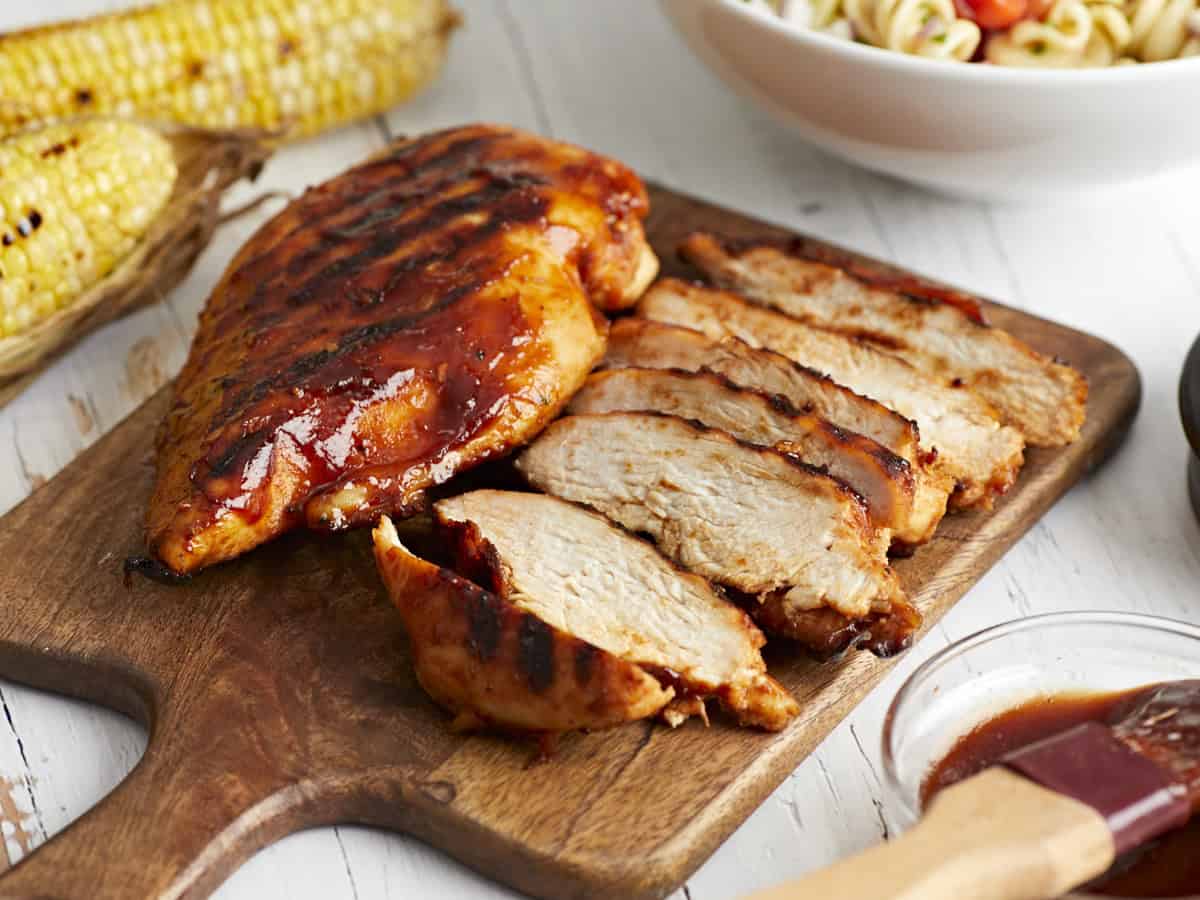 sliced grilled bbq chicken breast on a wood cutting board.