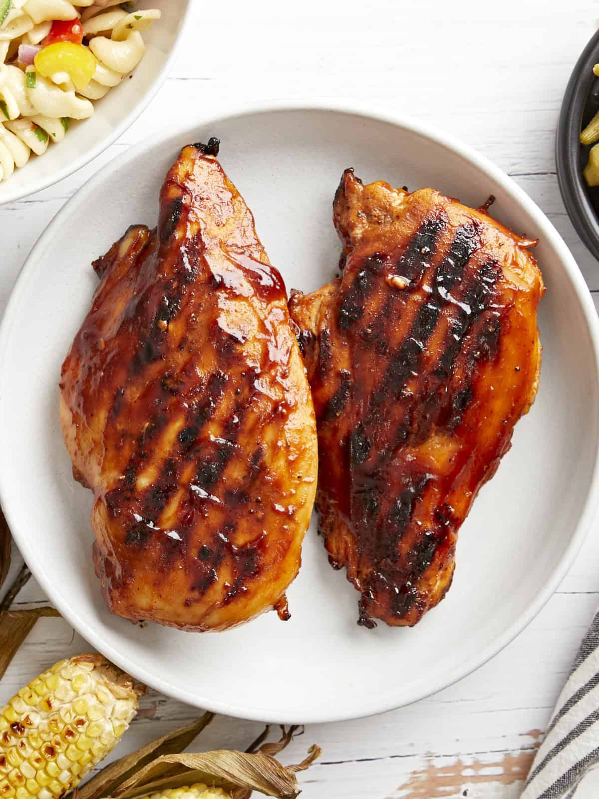 overhead view of 2 grilled bbq chicken breasts on a white plate.