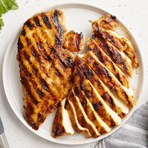 overhead view of 2 sliced grilled chicken breasts on a white plate.