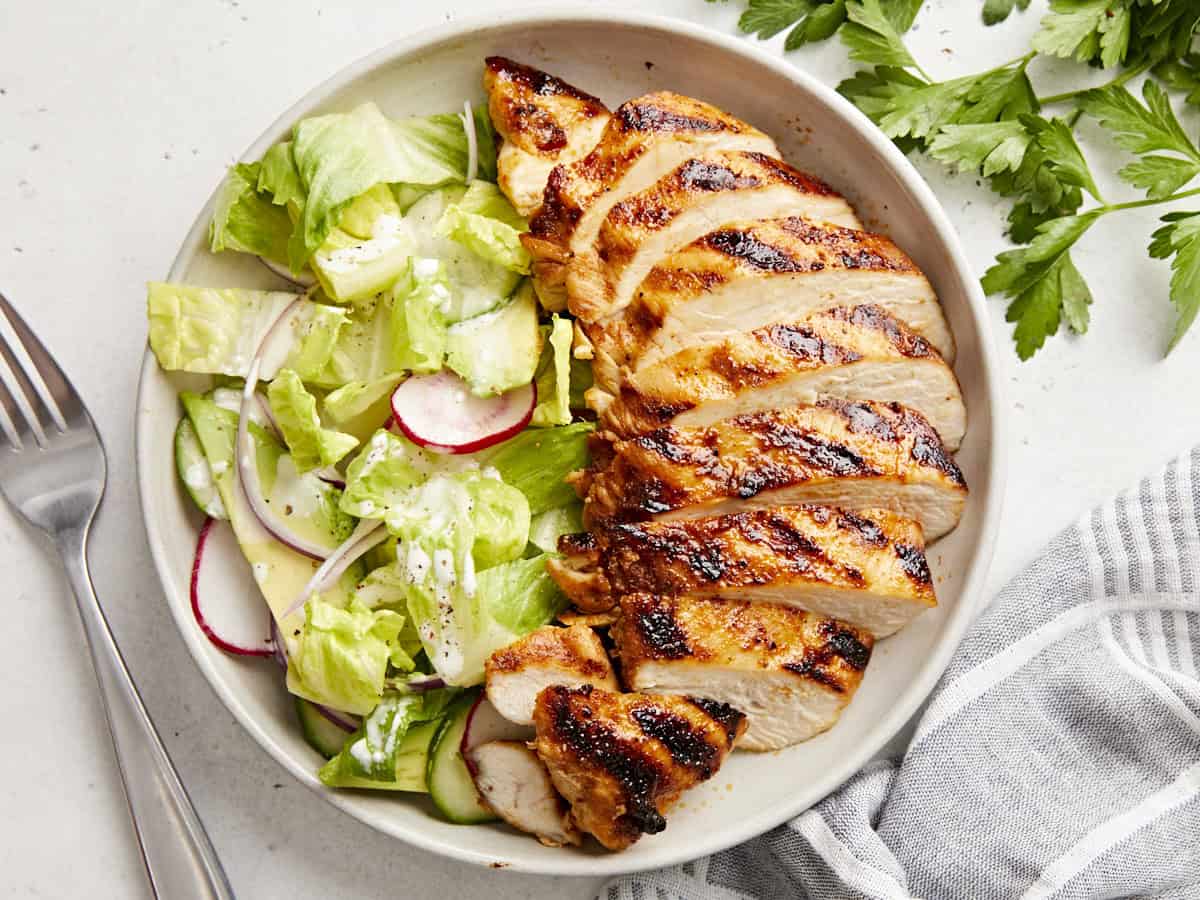 overhead view of a sliced grilled chicken breast on a plate with salad.