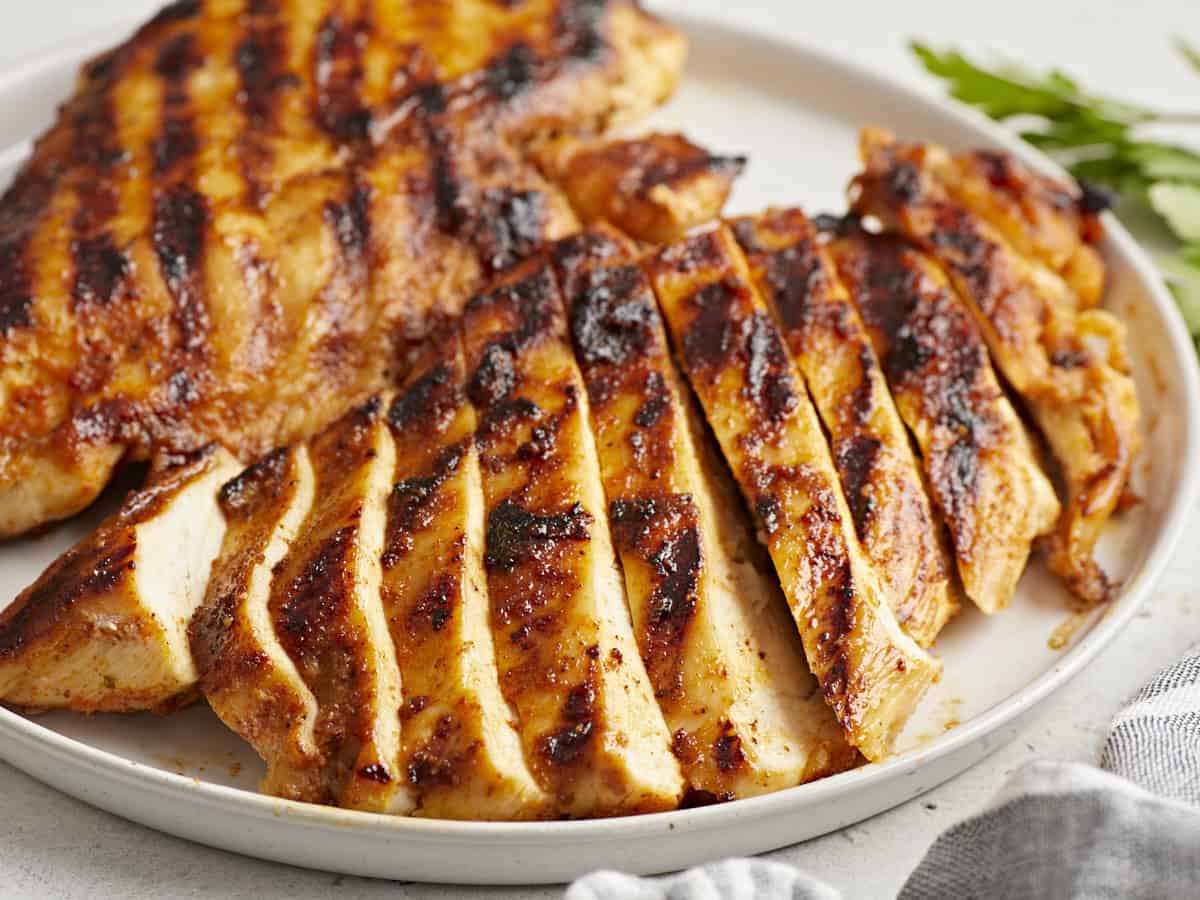 close up of sliced grilled chicken breasts on a white plate.