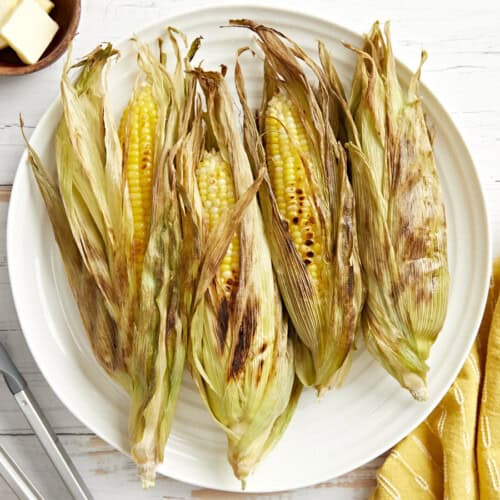overhead view of 4 ears of grilled corn on a white plate.