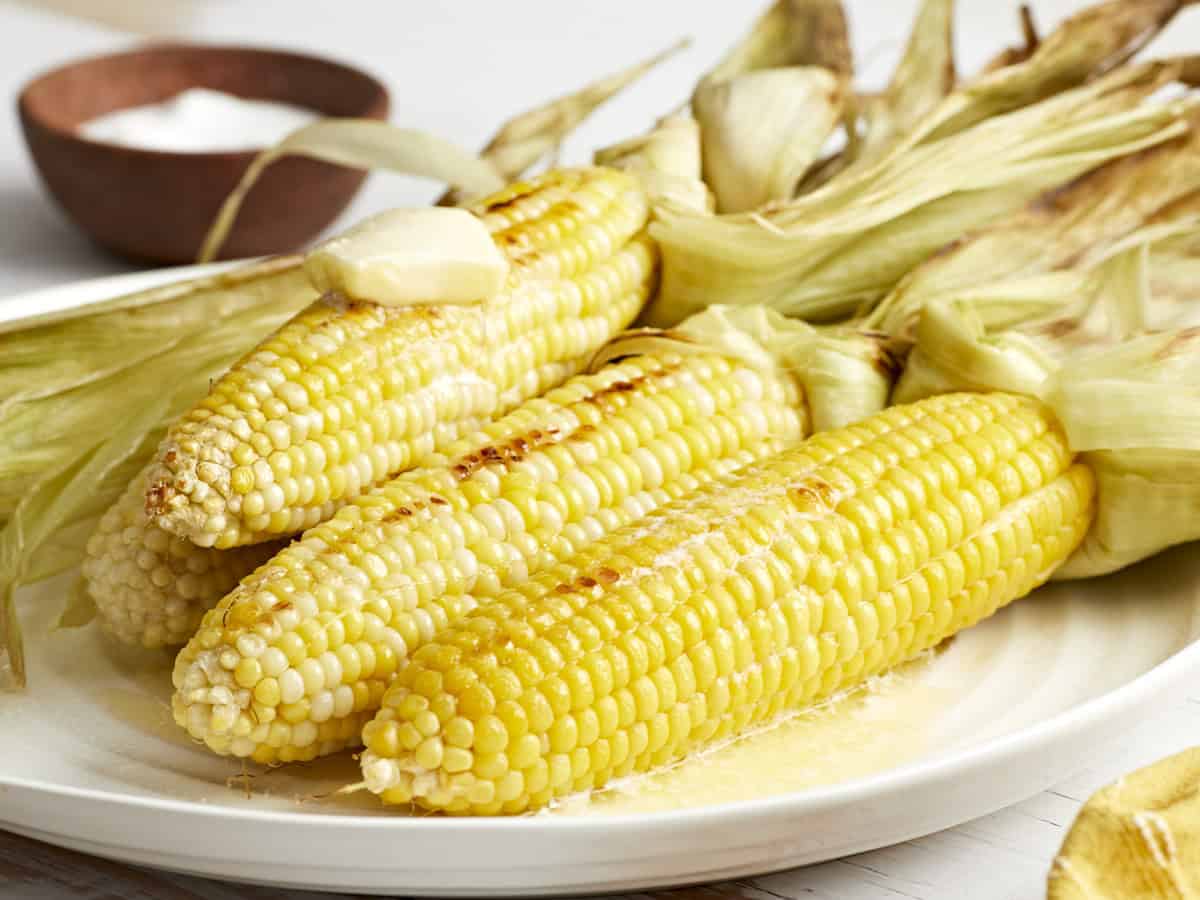 4 peeled ears of grilled corn with butter on a white plate.