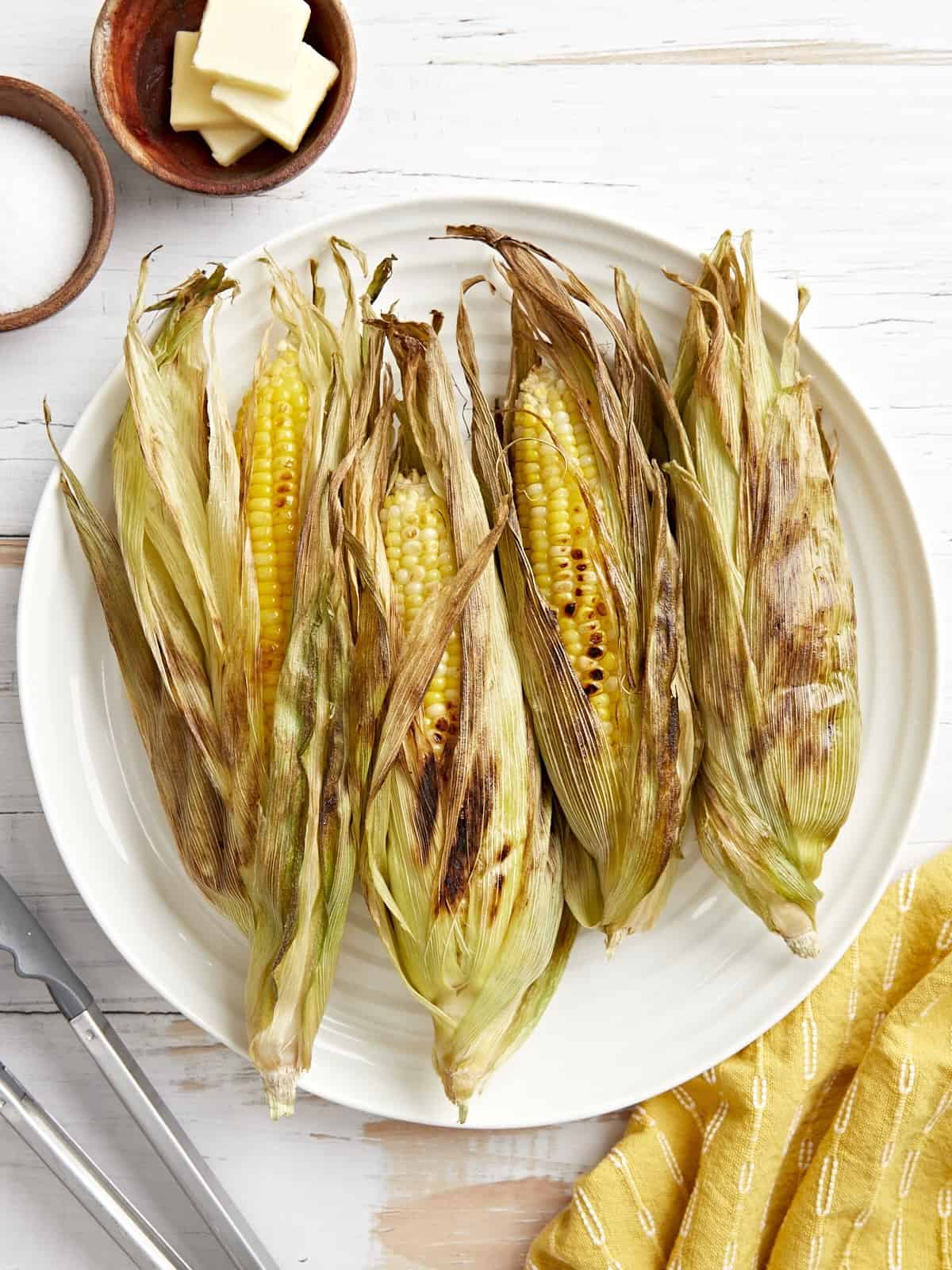overhead view of 4 ears of grilled corn on a white plate.