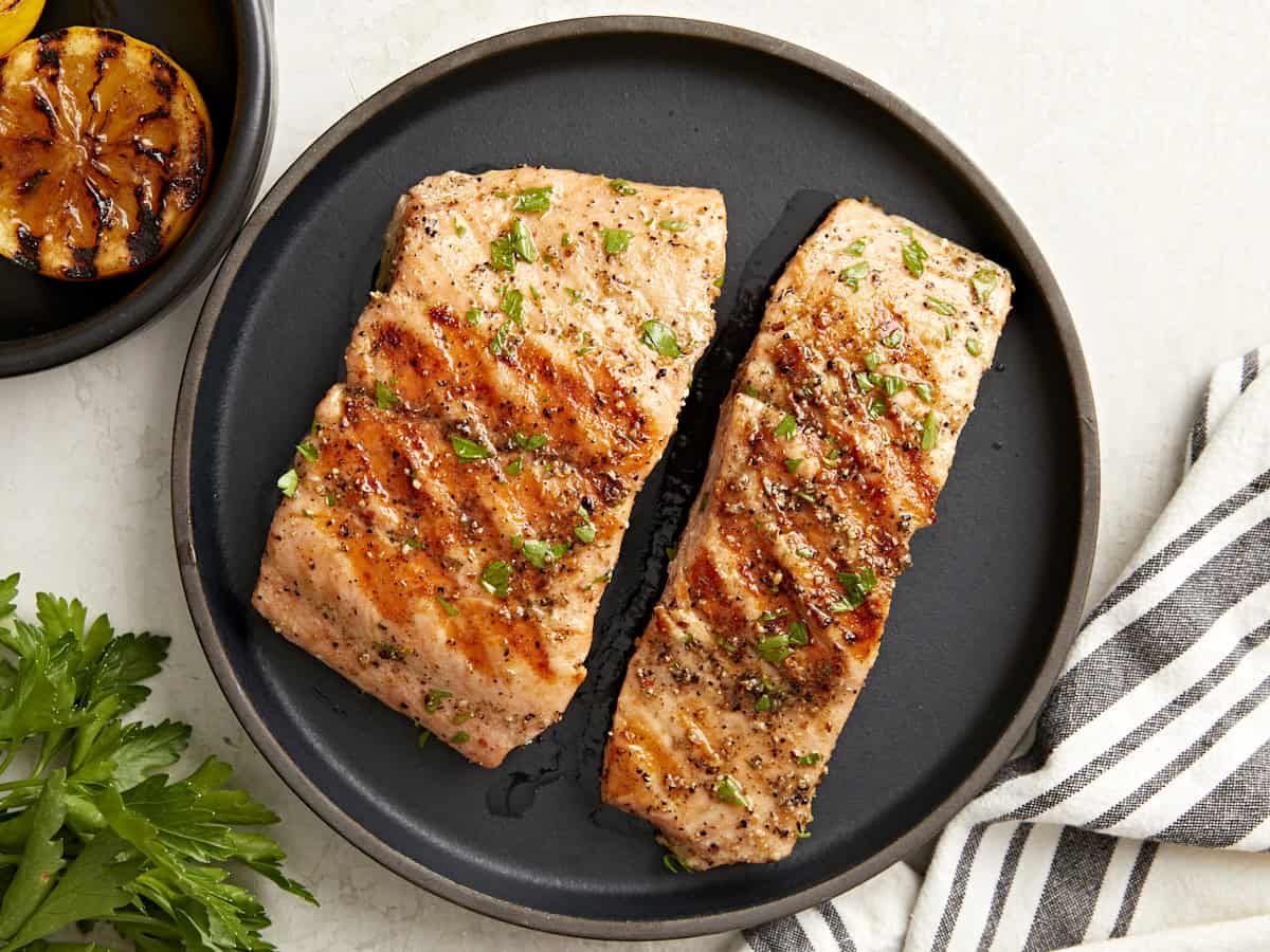 overhead view of 2 grilled salmon fillets on a black plate.