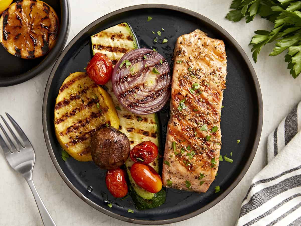 overhead view of a serving of grilled salmon and grilled vegetables on a black plate.