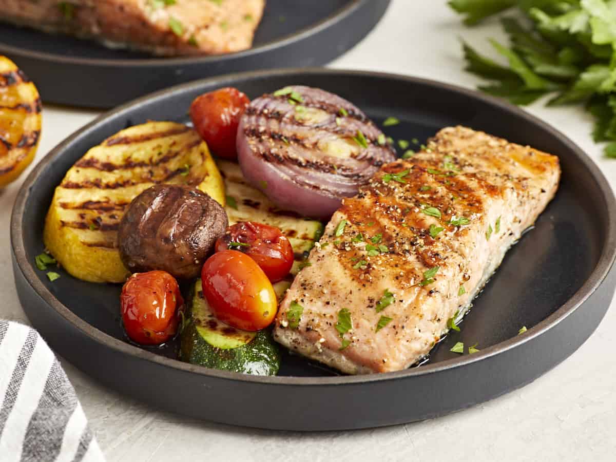a serving of grilled salmon and grilled vegetables on a black plate.