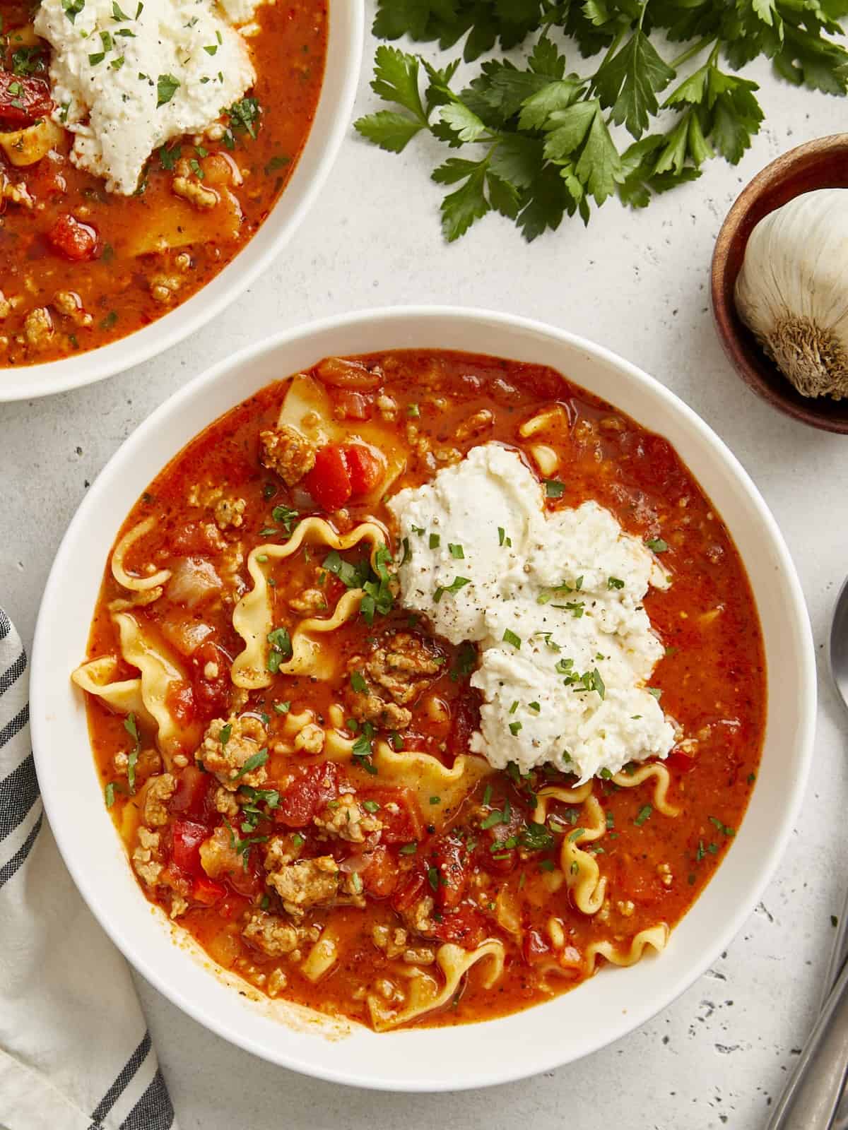 Overhead view of lasagna soup in a white bowl with ricotta cheese mixture on top.