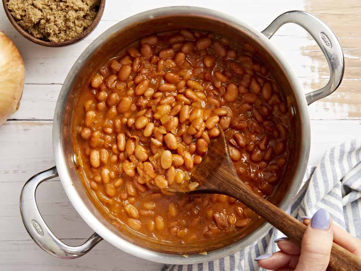 stirring a pot of stovetop baked beans with a wooden spoon.
