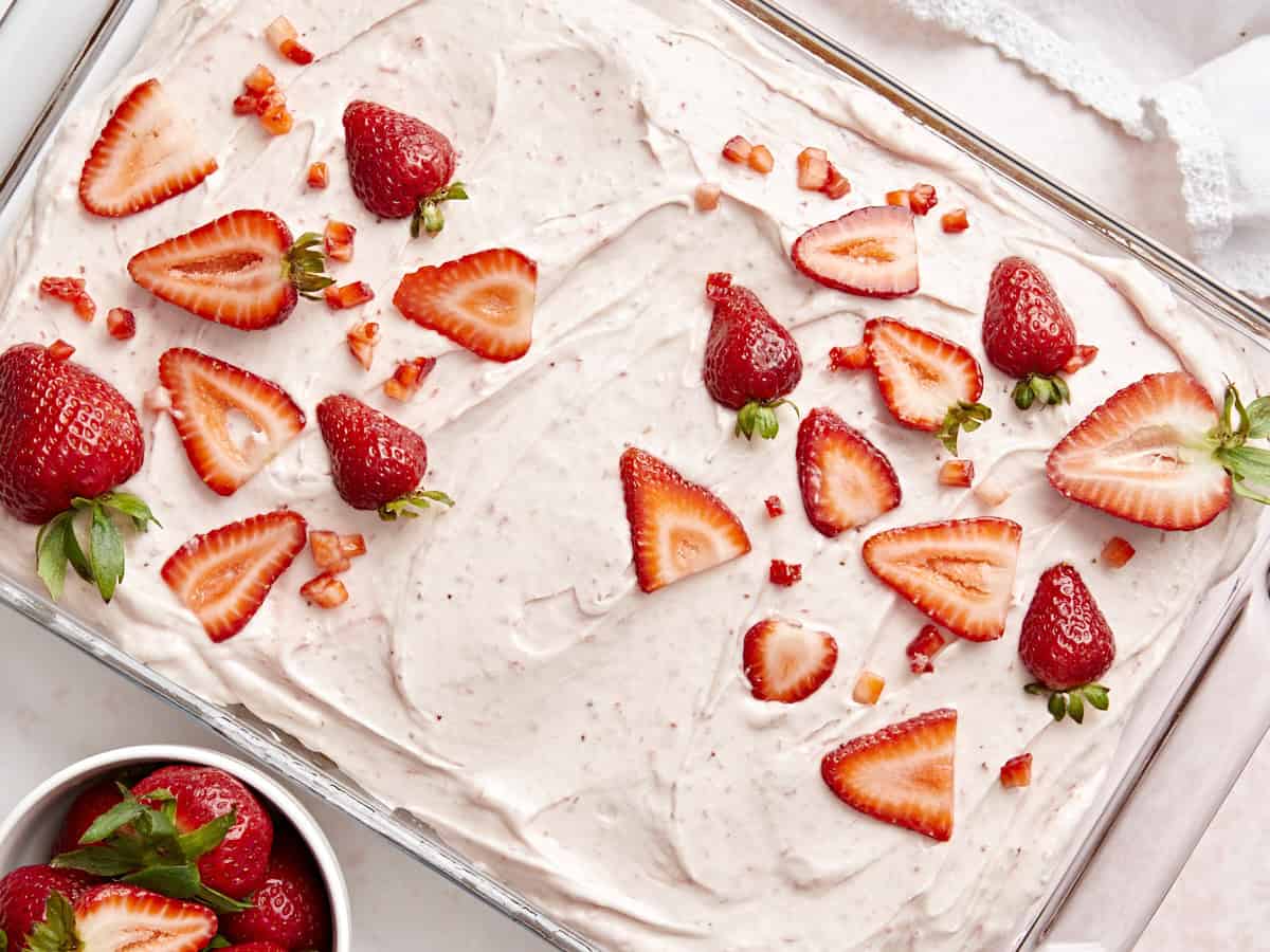 Overhead view of strawberry sheet cake with strawberry icing and fresh strawberries on top.
