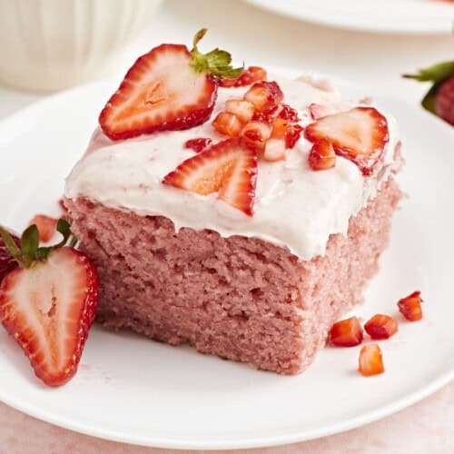 Close up view of strawberry sheet cake on a white plate with fresh strawberries on top.