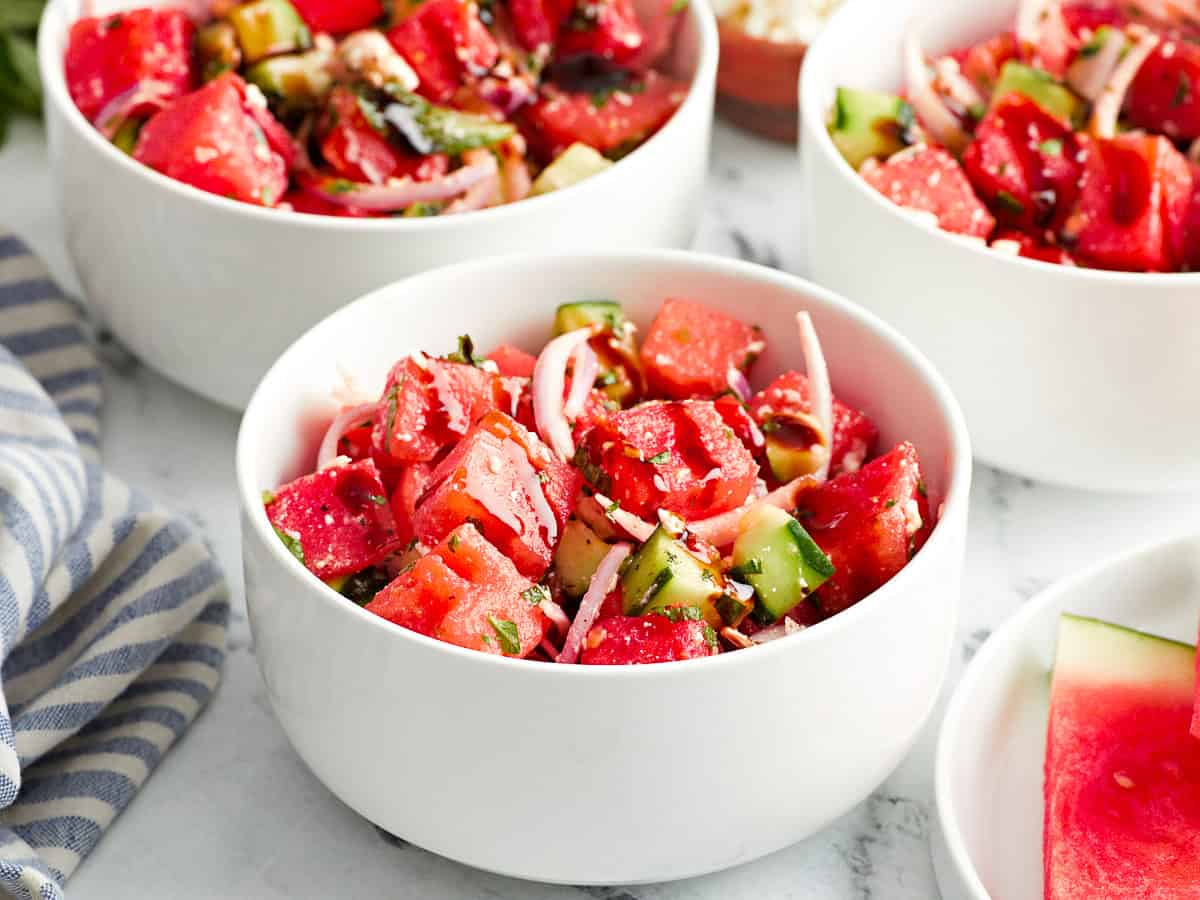 side view of servings of watermelon and feta salad in white bowls with balsamic glaze.