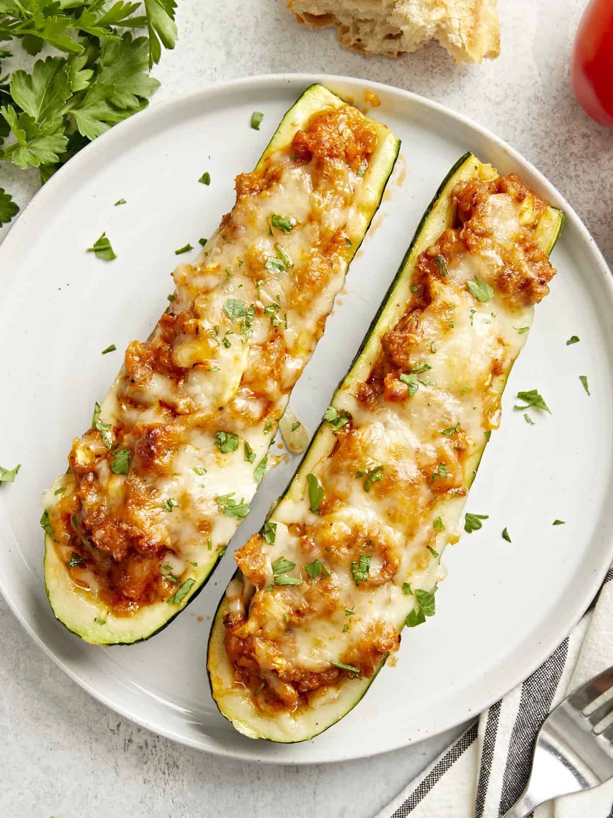 Two zucchini boats on a serving plate with parsley garnished on top.