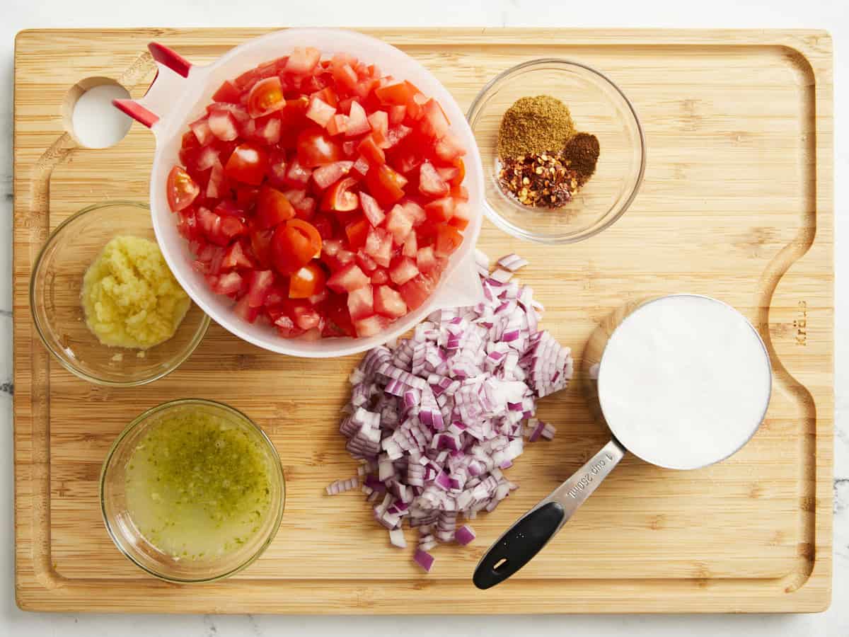 Ingredients for tomato relish on a wooden cutting board.